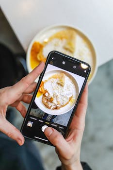 Hands using smartphone to capture an image of pancakes with powdered sugar.