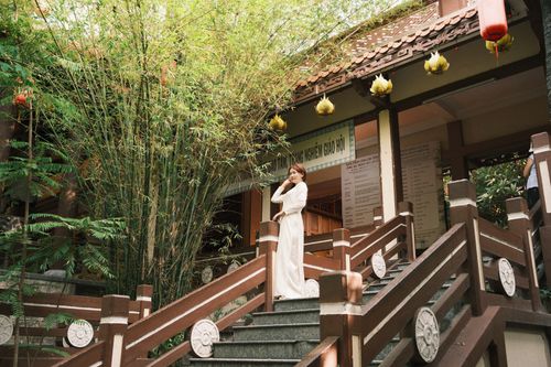 Free A woman in traditional attire poses gracefully on the stairs of a temple under lush foliage. Stock Photo