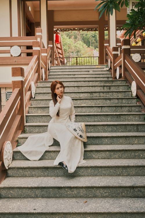 Free A woman in traditional clothing sitting on stone steps holding a conical hat. Stock Photo