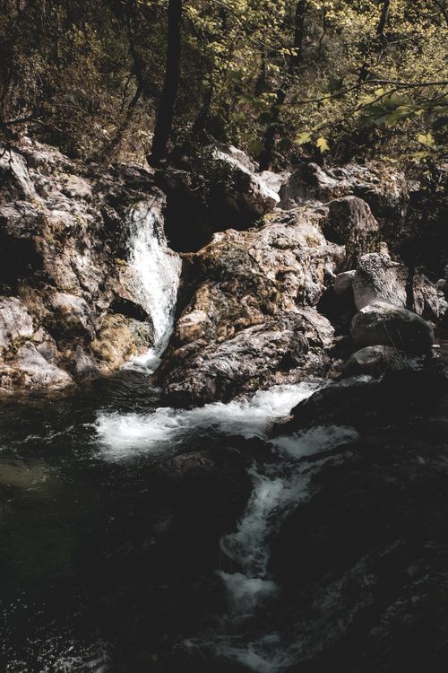Free A tranquil waterfall flows through a rocky forest landscape, showcasing nature's beauty. Stock Photo