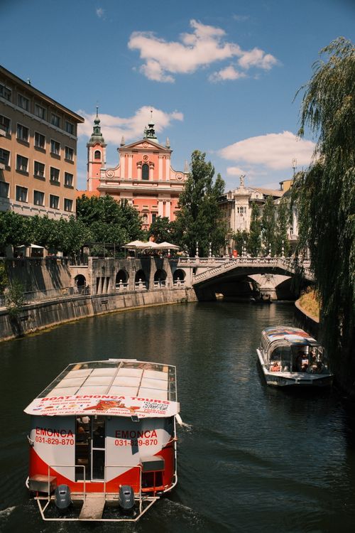 Free Scenic view of boats on Ljubljana River with the iconic pink Franciscan Church. Stock Photo