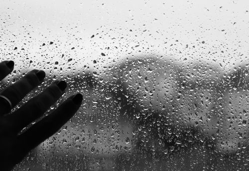 Free Artistic black and white photo of a hand touching a window covered with raindrops, creating a moody atmosphere. Stock Photo