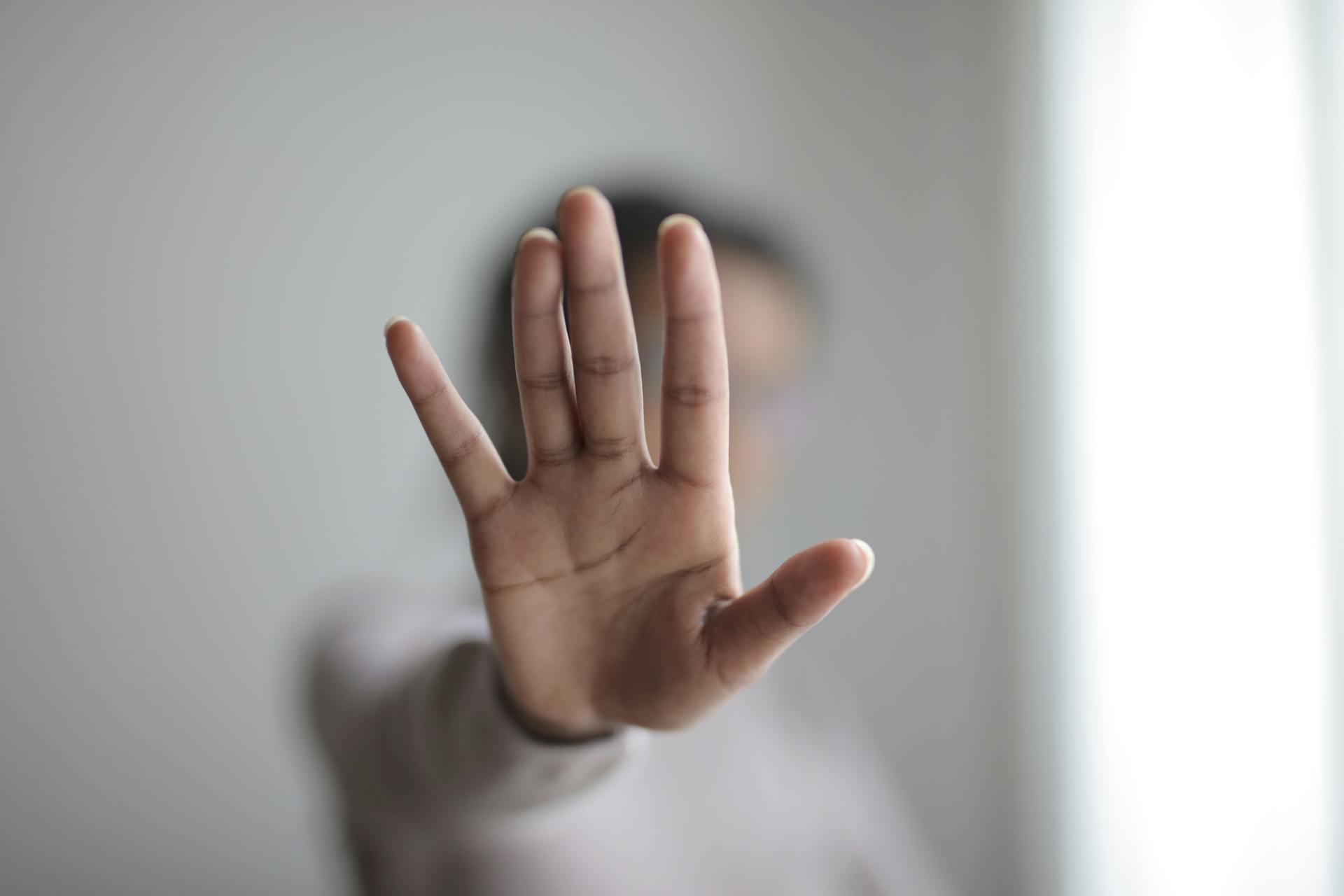 Blurred background with a close-up of an open hand, conveying a stop or pause gesture.