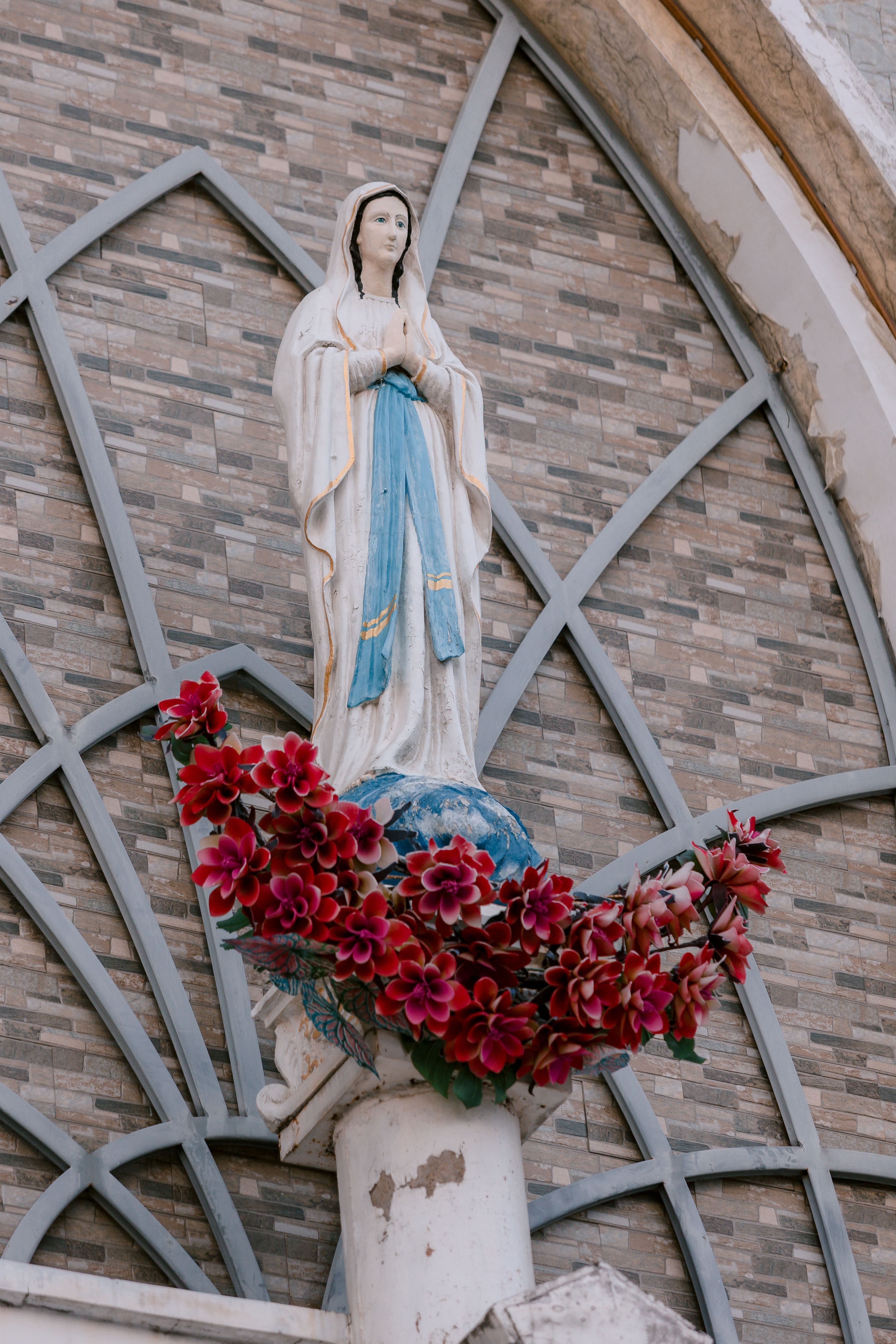 A statue of the Virgin Mary adorned with red flowers on a brick wall facade.