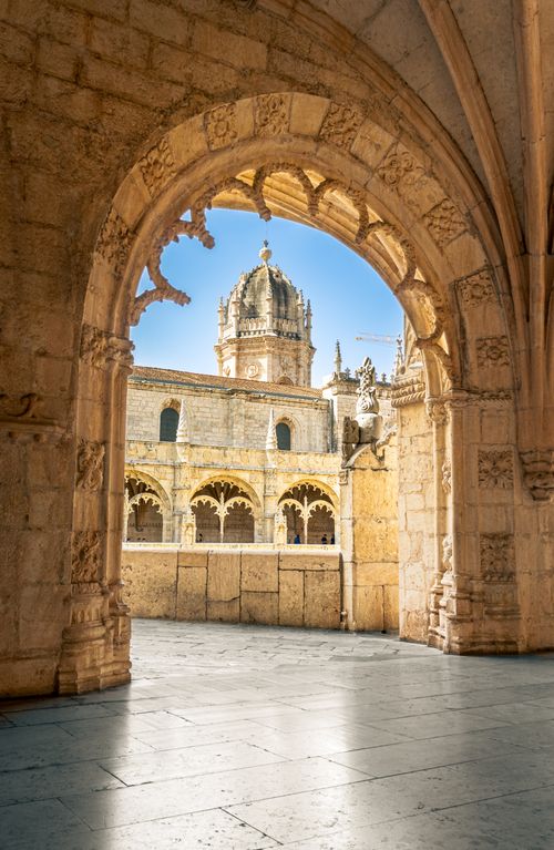 Free Sunlit view of Jerónimos Monastery's cloister through archway, Lisbon, Portugal. Stock Photo