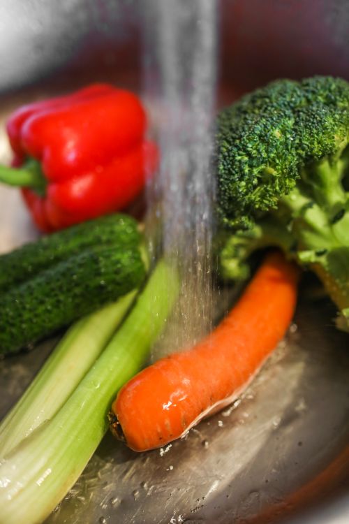 Free Fresh broccoli and pepper and celery with cucumber and carrot placed in metal bowl under running water in modern kitchen Stock Photo