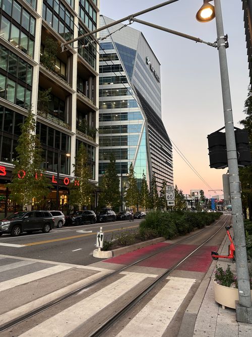 Free A vibrant city street with a striking skyscraper and tram tracks at sunset, showcasing modern urban architecture. Stock Photo