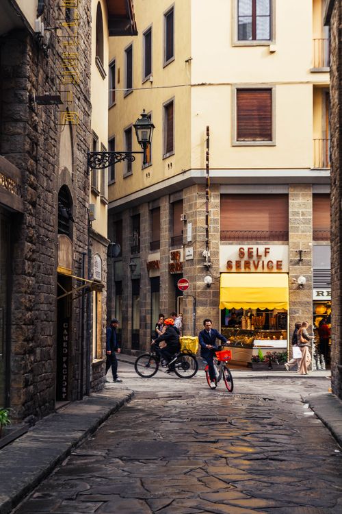 Free A bustling narrow street in Florence with cyclists and a classic Italian self-service store. Stock Photo