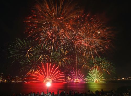 Free Stunning night fireworks show with vibrant colors over a city waterfront, celebrating a festive occasion. Stock Photo