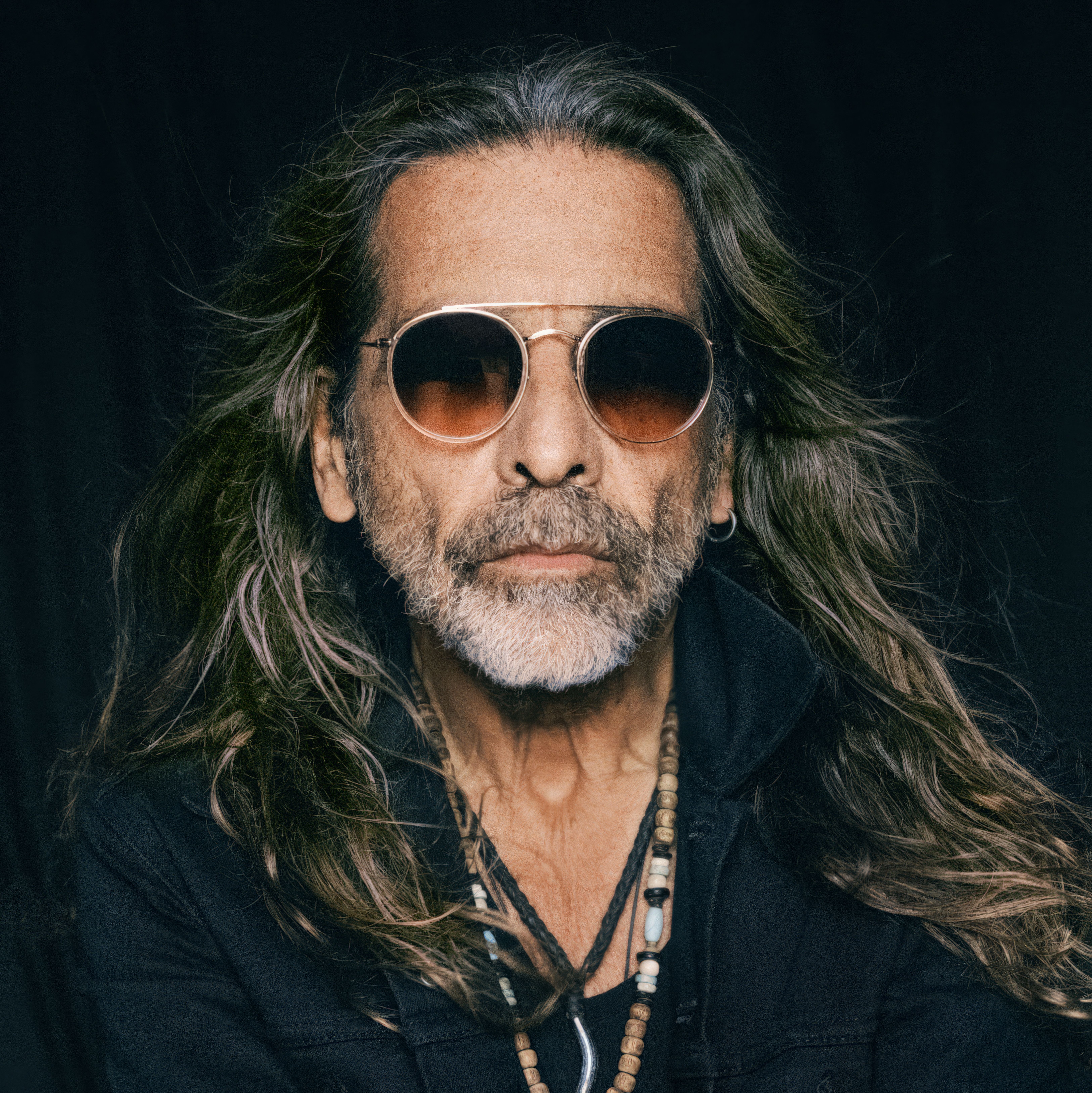 Elderly man with long hair and sunglasses in a fashionable portrait.