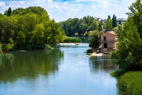 Free A tranquil river scene with a rustic building, lush greenery, and clear skies. Stock Photo
