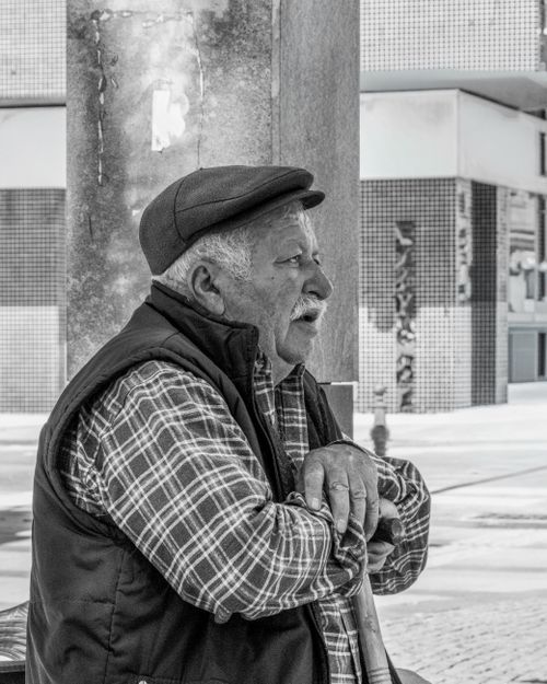 Free Black and white photo of a senior man resting on a cane outdoors, wearing a cap and plaid shirt. Stock Photo