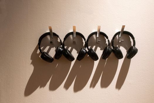 A row of four black headphones hanging neatly on wall hooks casting shadows.
