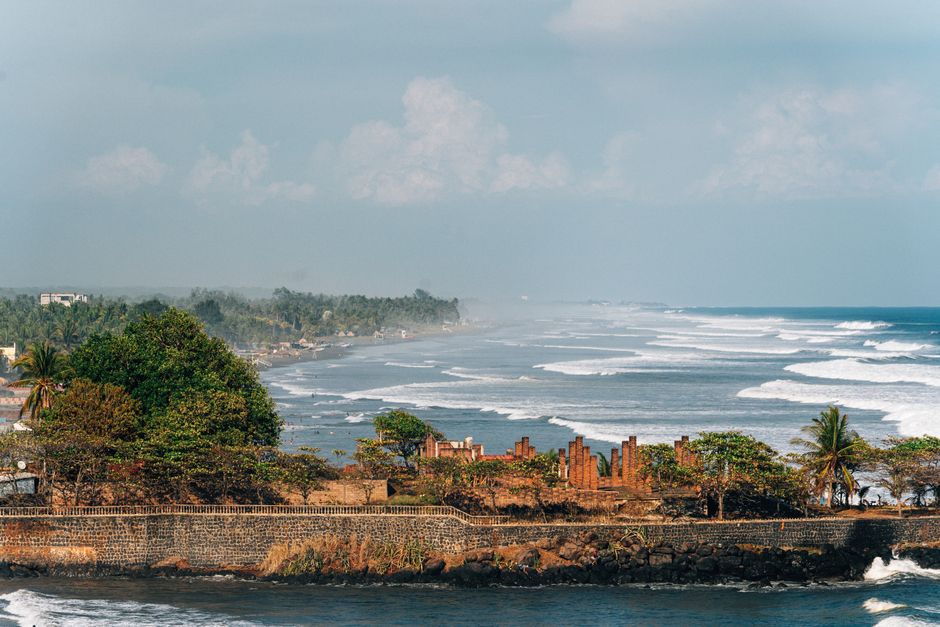 Picturesque view of a coastline with lush greenery and waves under a blue sky.