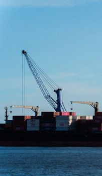 View of a commercial shipping port with cranes and stacked cargo containers against a clear sky.