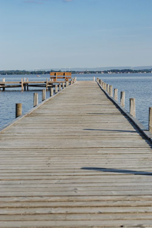 Free A serene wooden pier stretches over a peaceful lake in Wunstorf, Germany, under a clear blue sky. Stock Photo
