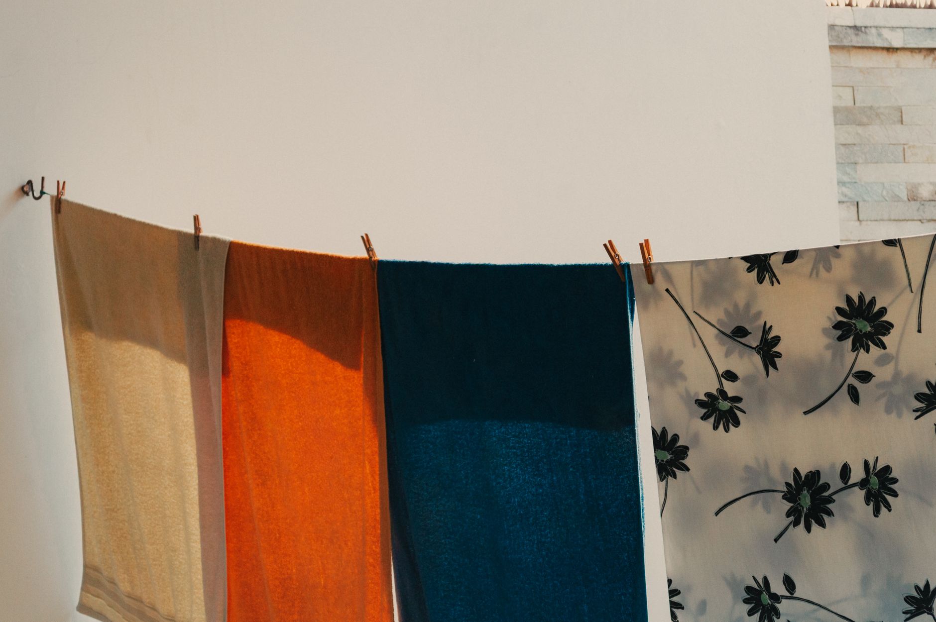Four colorful towels drying on a clothesline against a white wall, creating a vibrant scene.