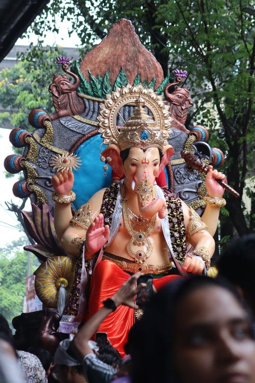 Free Vibrant idol of Lord Ganesh during outdoor festival procession, surrounded by people and lush greenery. Stock Photo