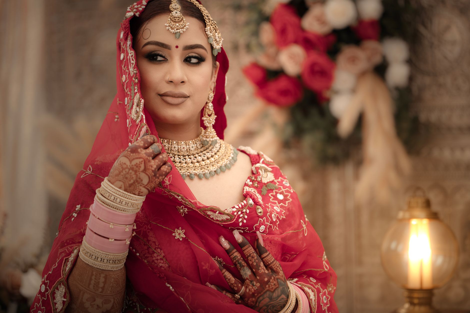 Beautiful bride in red sari with intricate henna and jewelry, posing indoors.