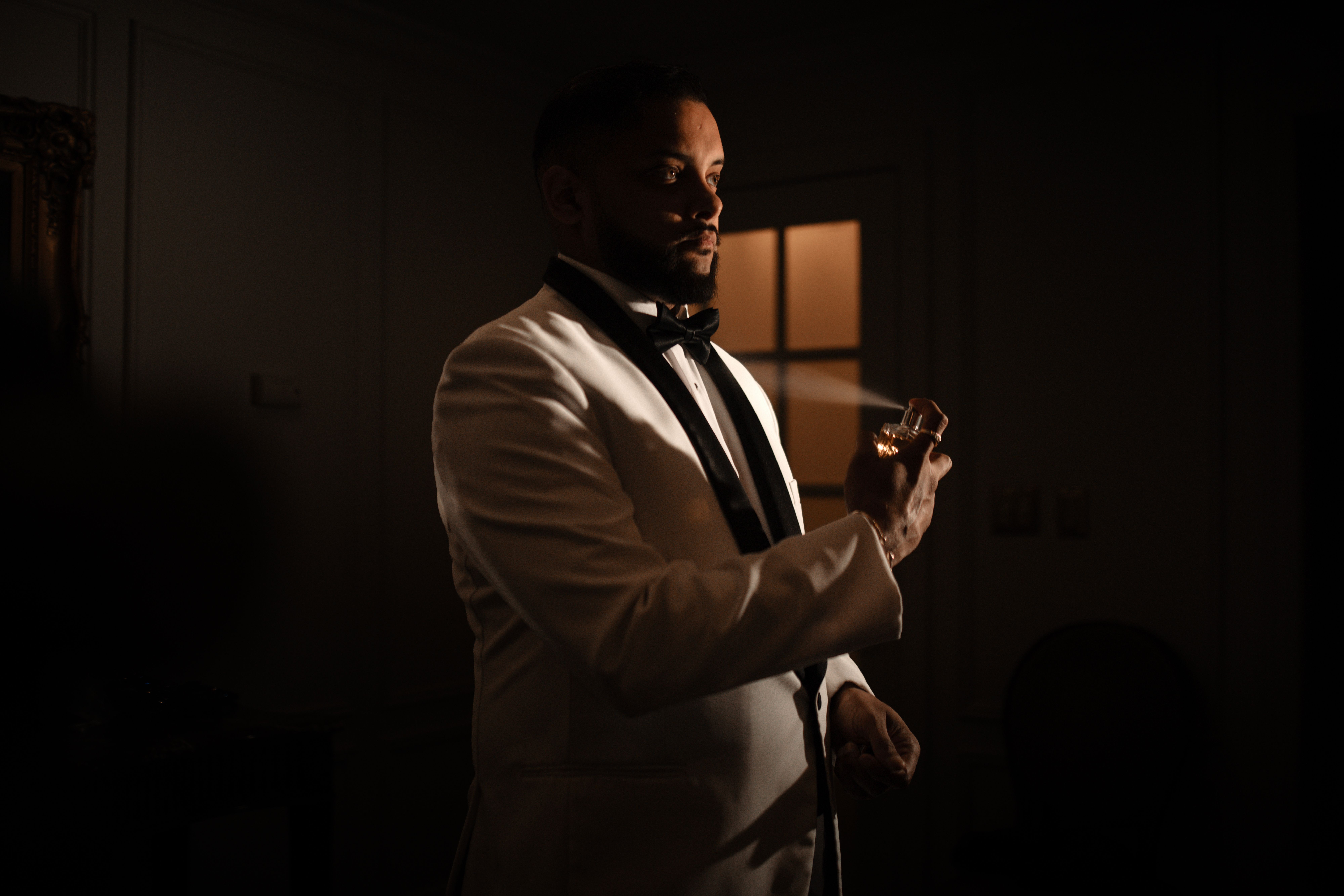 Sophisticated man in a tuxedo sprays fragrance indoors. Luxurious and elegant atmosphere.