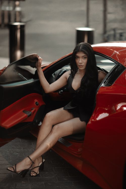 Free Elegant woman in black dress seated in a red sports car, exuding style and luxury. Stock Photo
