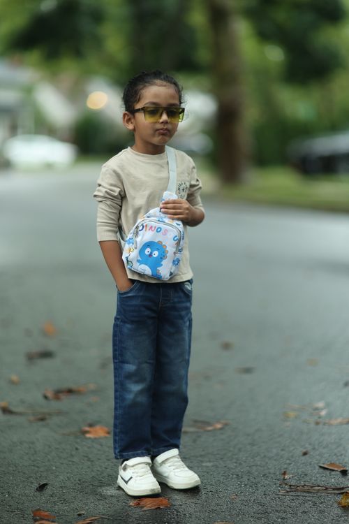 Free Young boy in casual outfit with sunglasses and sling bag standing on a street. Stock Photo