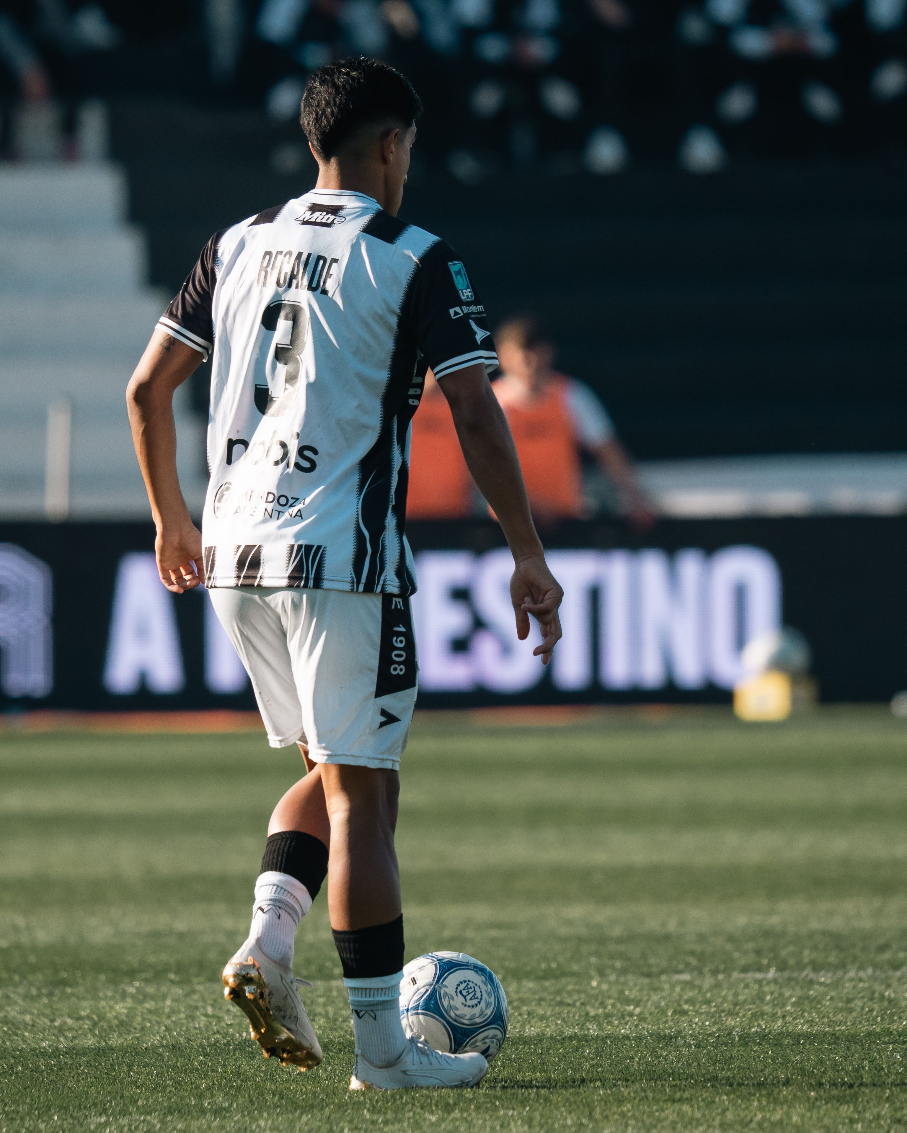 Soccer player in uniform on the field during a daytime match, preparing to kick the ball.