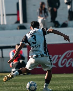 A soccer player kicks a ball during an outdoor match on a sunny day.