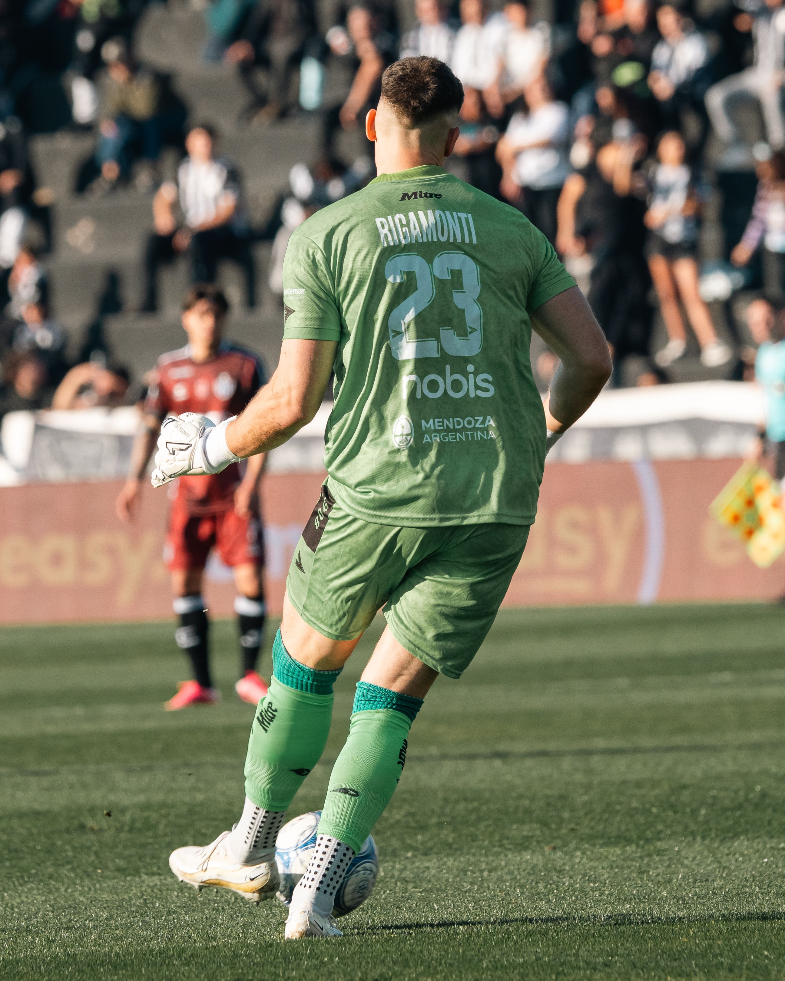 Goalkeeper preparing to kick the ball during a lively soccer match on a sunny day.