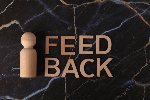 Wooden letters spelling 'FEEDBACK' on a dark marble surface with a wooden figure.