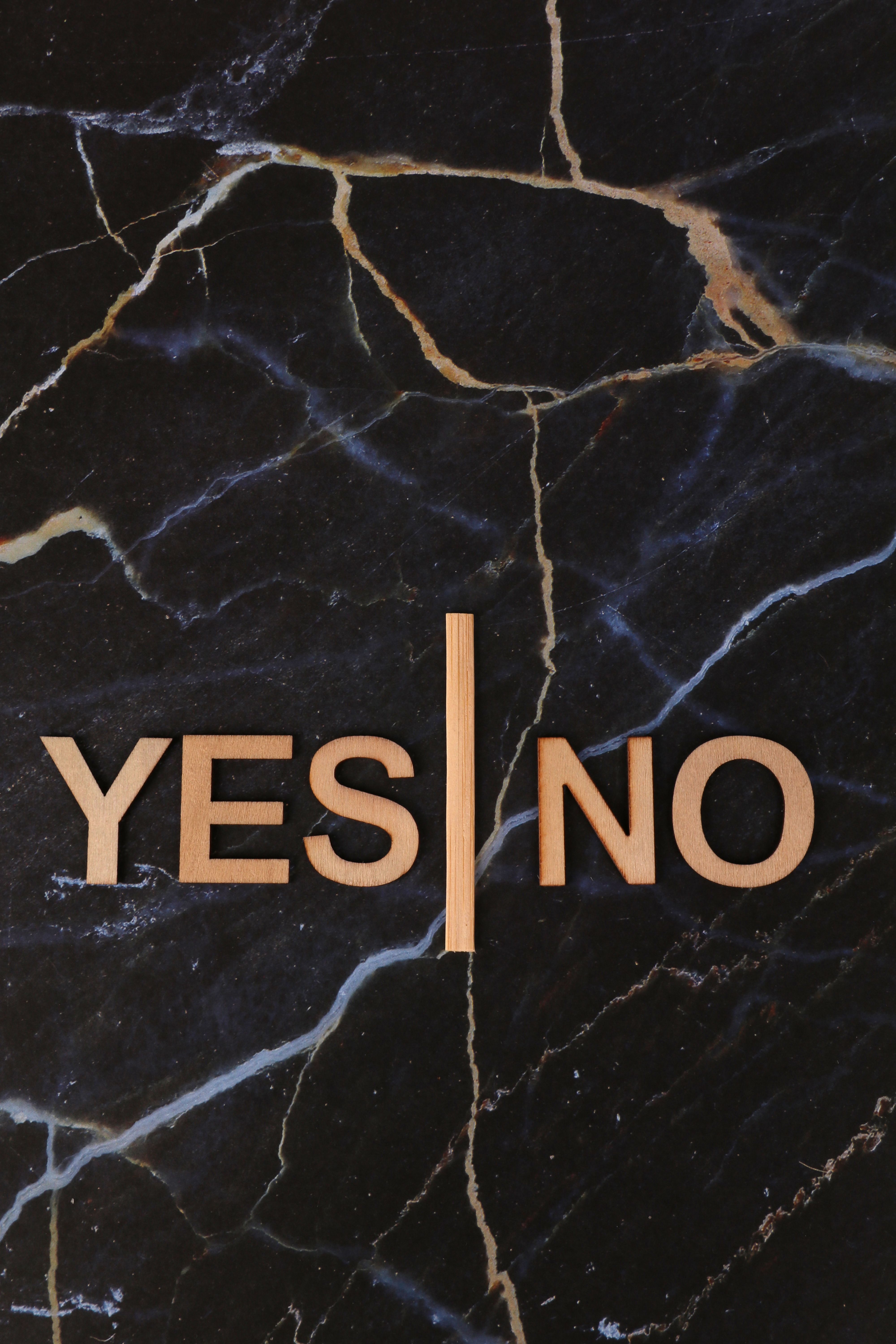 Wooden letters spelling Yes and No on black marble background, symbolizing decision-making.