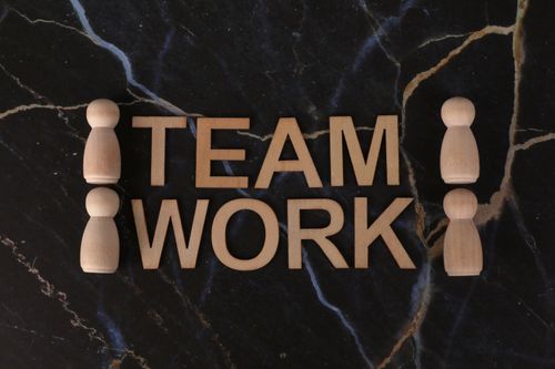 Free Wooden figures symbolize teamwork on a dark marble background, emphasizing collaboration. Stock Photo