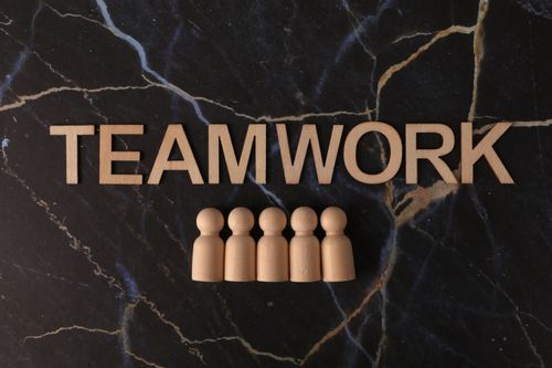 Free Wooden figures arranged under 'TEAMWORK' on a marble background symbolizing collaboration. Stock Photo