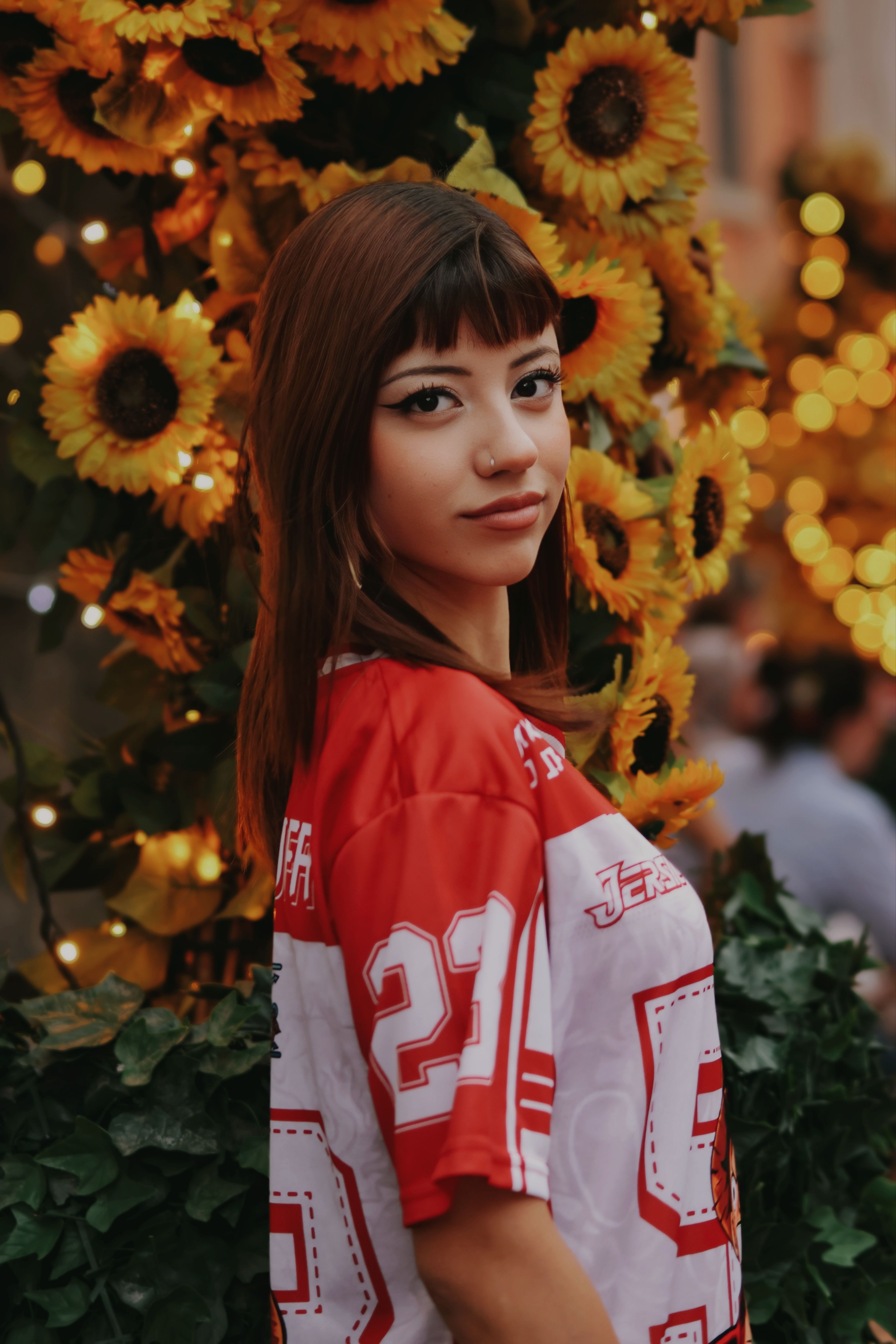 Young woman in sports jersey surrounded by vibrant sunflowers, warm evening glow.