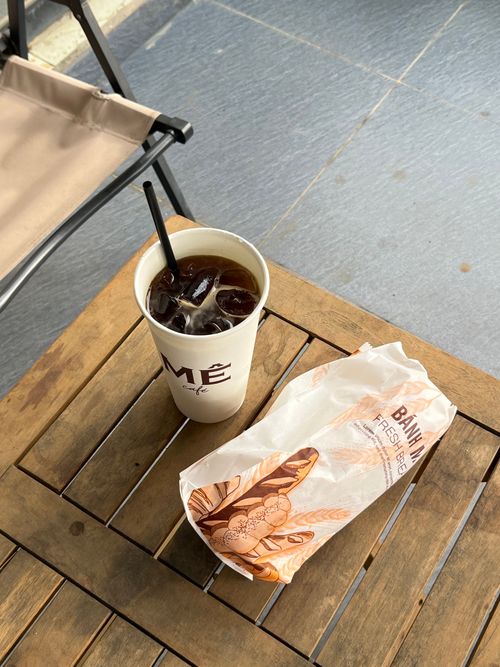 Free Iced coffee and a wrapped banh mi sandwich on an outdoor wooden table. Perfect for a quick and refreshing break. Stock Photo