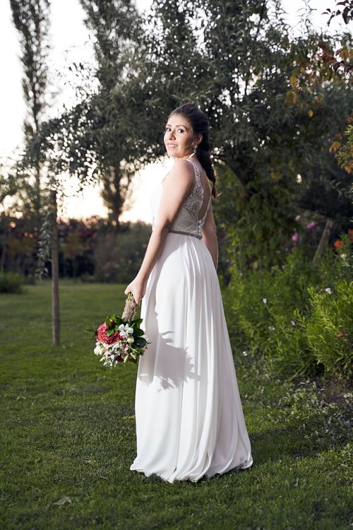 Free Elegant bride in white gown holding bouquet in scenic garden setting during golden hour. Stock Photo