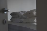 透过打开的门，可以看到一个宁静的卧室场景，床上堆放着枕头和折叠起来的毯子