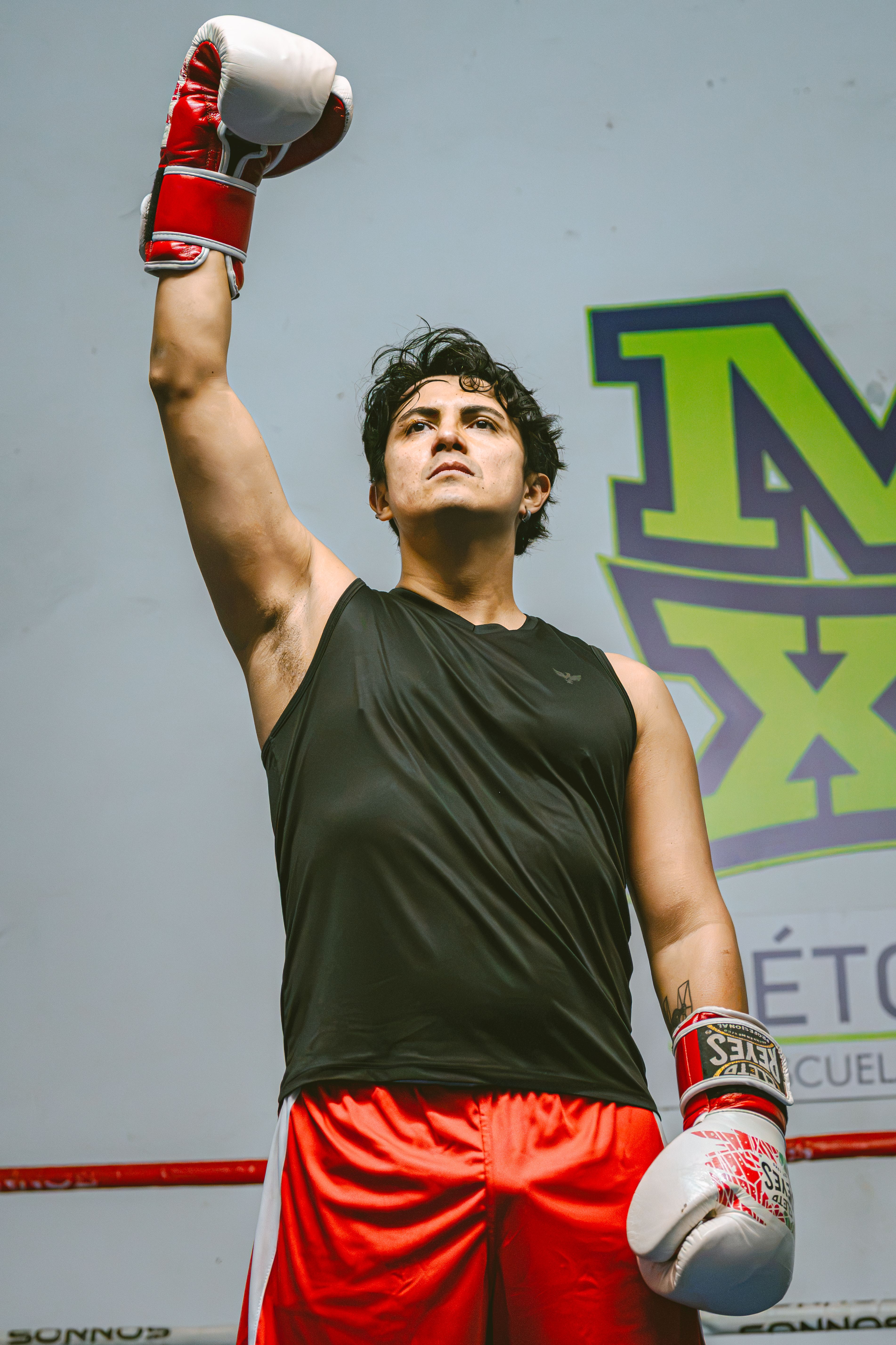 A determined boxer in a victory pose with raised arm inside a boxing ring.