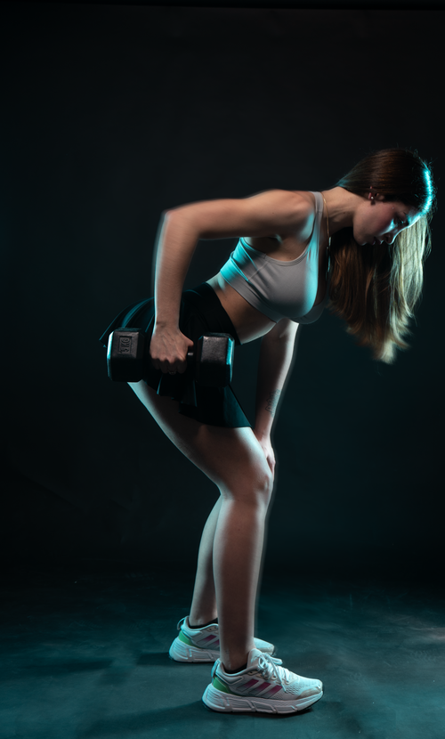 Free A young woman performing a dumbbell workout in a studio setting, showcasing strength and fitness. Stock Photo