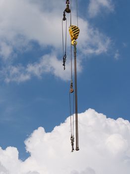 Close-up of crane machinery with hooks and cables against a cloud-filled sky.