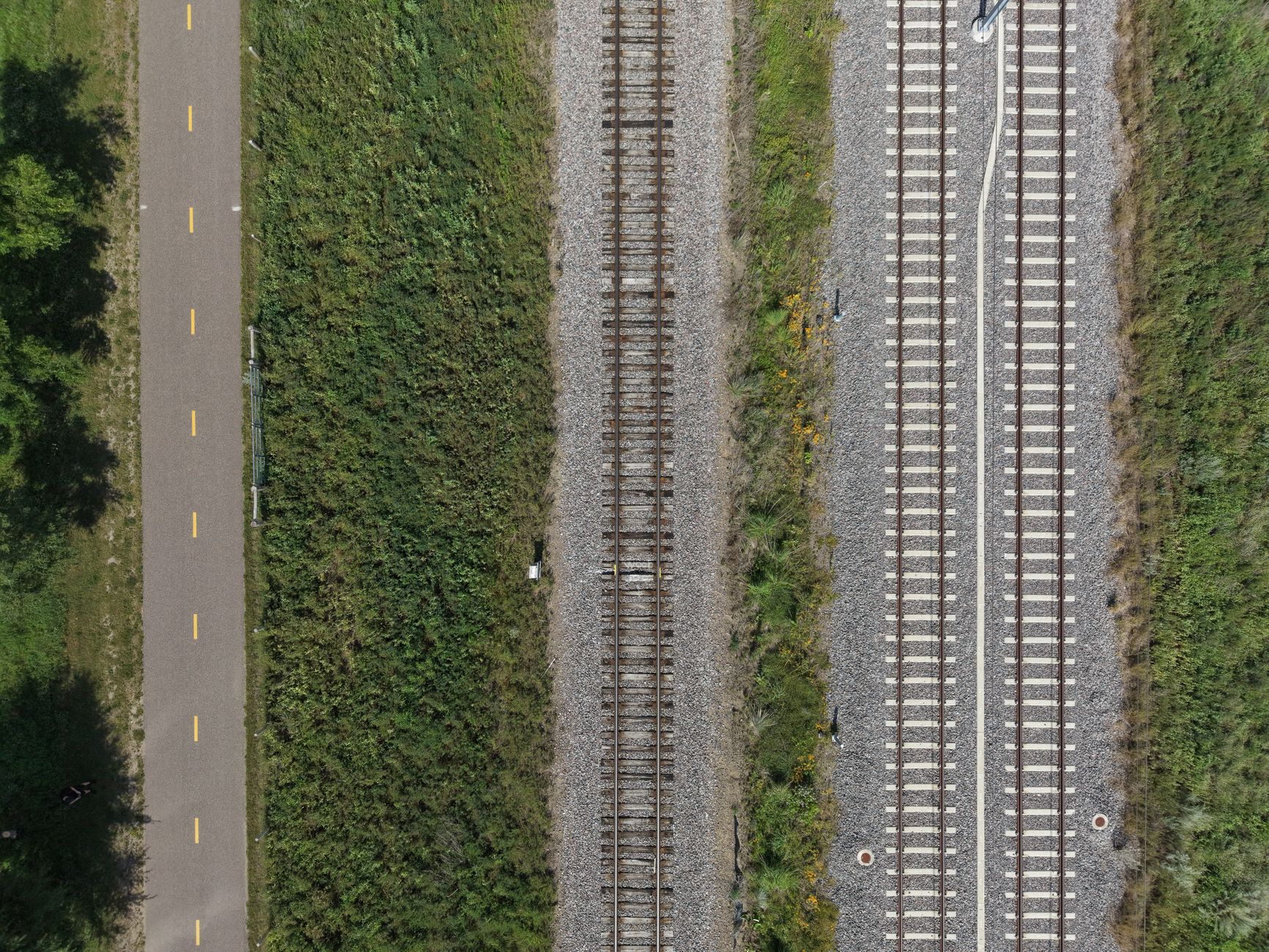 Top-down aerial shot of railway tracks and adjacent bike path with greenery.