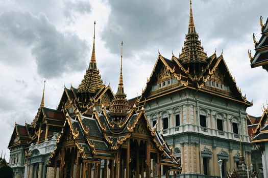 A beautiful view of the ornate rooftops of the Grand Palace in Bangkok, Thailand, under a cloudy sky.
