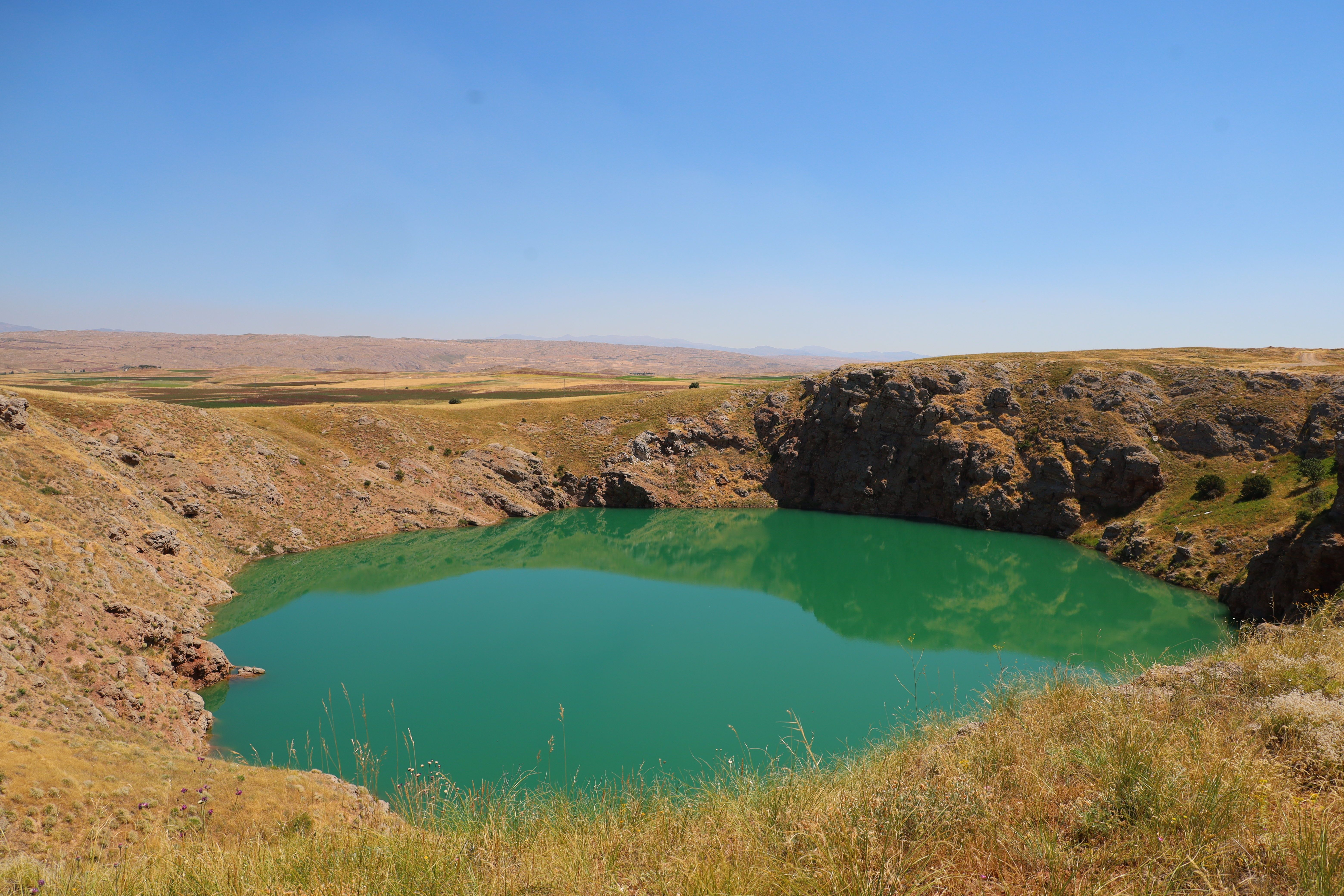 A vibrant crater lake surrounded by rugged terrain under a clear sky.