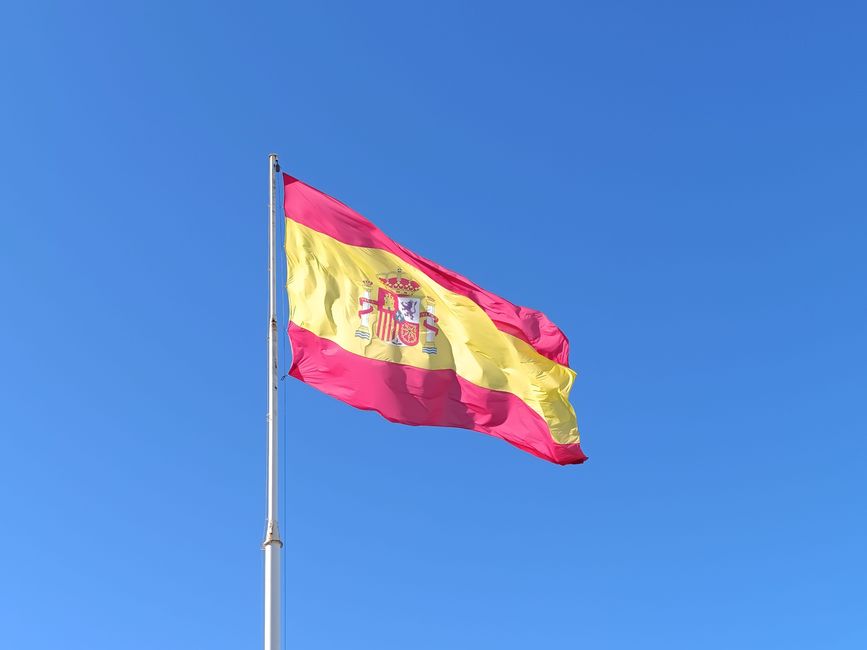 Vibrante bandera española ondeando bajo un cielo azul claro, simbolizando el orgullo nacional en España.