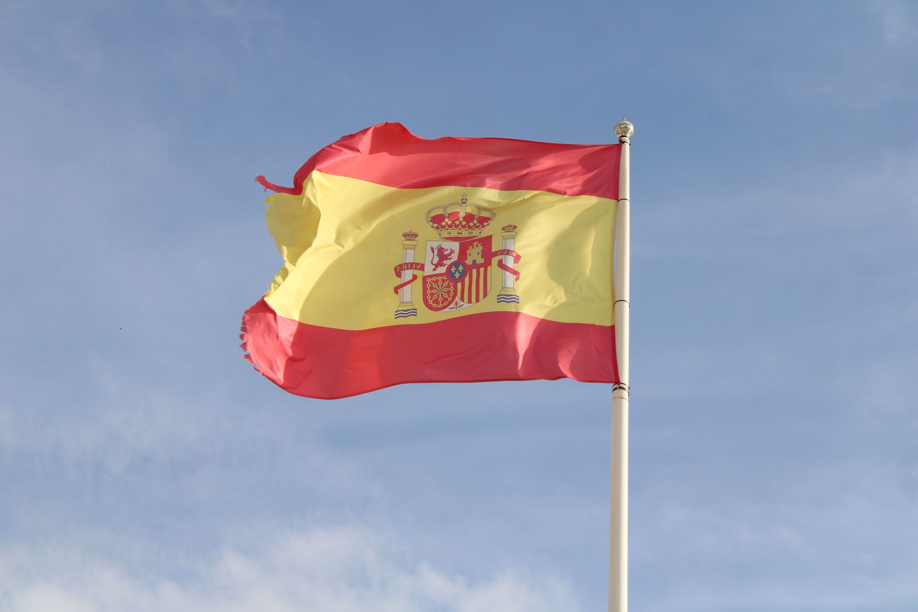 The Spanish national flag fluttering against a bright blue sky symbolizing national pride.