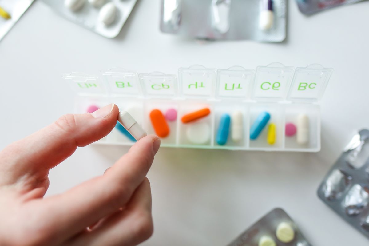Close-up of a hand selecting a pill from a weekly organizer, illustrating a five-day Xocova course