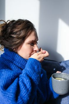 一位穿蓝色毛衣的女性正用热饮服药，表现出流感症状