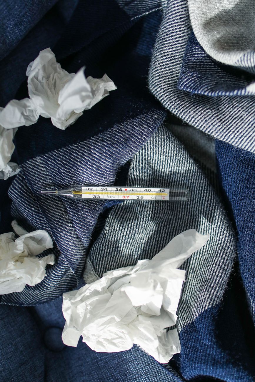 A glass thermometer and crumpled tissues lying on a denim blanket during a cold