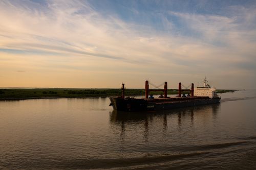 Free A large cargo ship navigates through a tranquil river under a dramatic sunset sky. Stock Photo