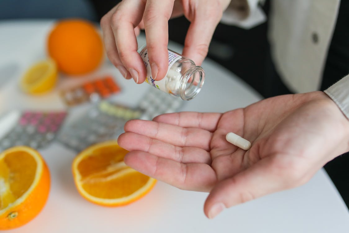 person pouring supplement capsules in palm of hand above a table with orange slices